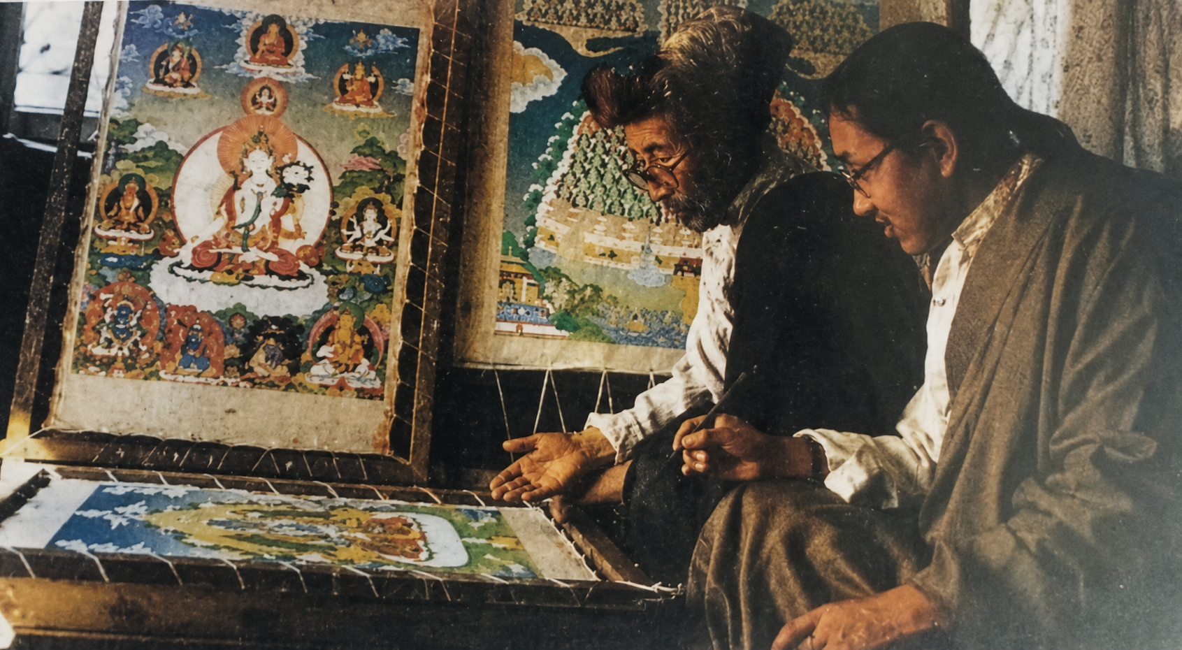 Master Jamphel Wangchuk and Master Tenzin Dhargay seated together beside Tibetan thangka paintings