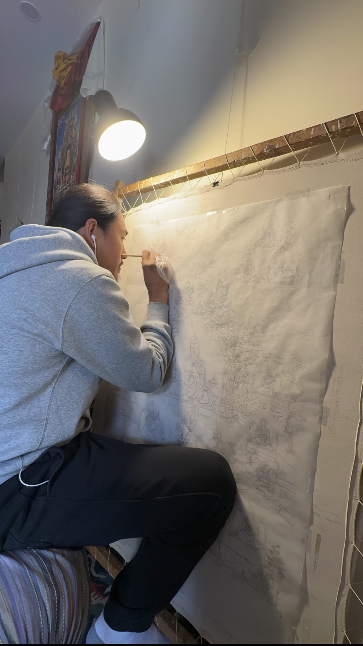 Tenzin Kalden preparing a measured thangka drawing beneath a studio lamp